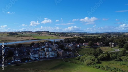 Aerial drone view flying along the village of Alnmouth in Northumberland showing buildings and roads along the river Aln and surrounding countryside