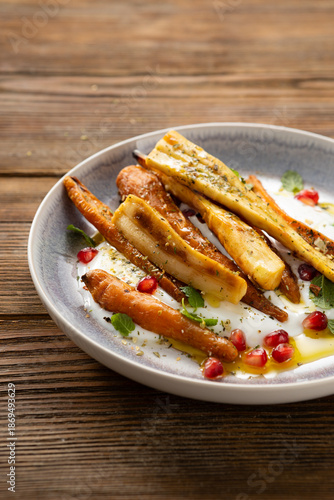 Roasted carrots and parsnips with greek yogurt on plate wood surface