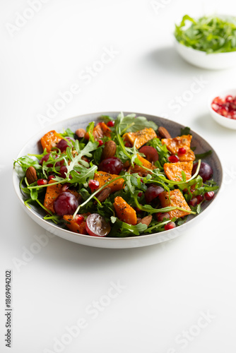 Fresh salad with roasted pumpkin and grapes on plate  light surface