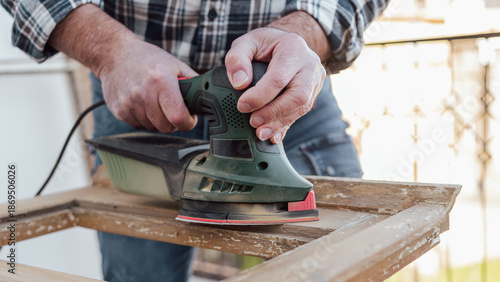 Craftsman. Adult carpenter using an electric sander to smooth an old wooden window. Construction industry, carpentry, housework do it yourself. Restoration.