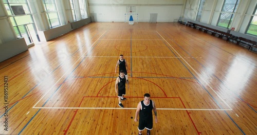 A coach goes to the center of the field and puts the ball into play. a team of four players play basketball on an indoor court.