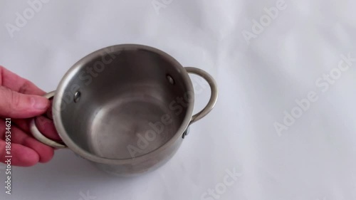 An empty stainless steel pot with side handles sits on a white surface - highlighting clean kitchenware, simple composition, and a calm moment in culinary preparation