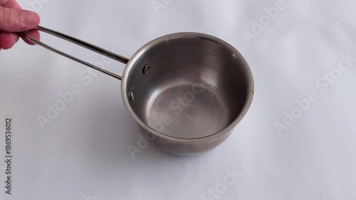 An empty stainless steel measuring cup with a long handle sits on a white surface - capturing clean kitchen tools, simple composition, and a quiet moment in culinary prep