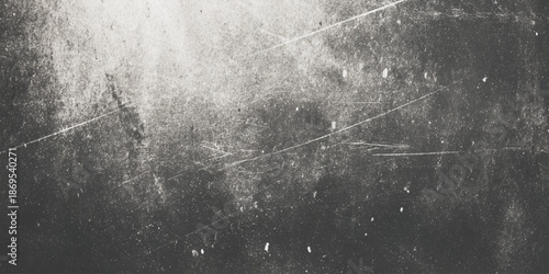 A grayscale abstract image featuring a textured surface with dark and light areas and scattered linear markings