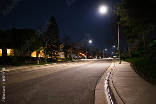 Obraz na plátně Quiet residential street at night in Corona, California, lit by streetlights with empty roadway, sidewalk, and suburban homes