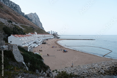 Beachfront buildings lining sandy bay with the rock of gibraltar rising behind, showing people enjoying the sand and sea