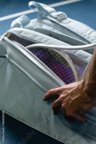 Close up of a male hand opening a tennis bag with racket inside on a blue court. Preparation for training or match, sports equipment and active lifestyle concept.