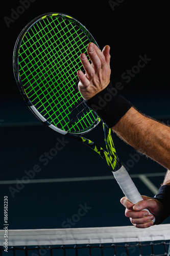 Close up of a male hand touching the strings of a tennis racket near the net on a blue court. Precision, technique and focus during professional tennis play.