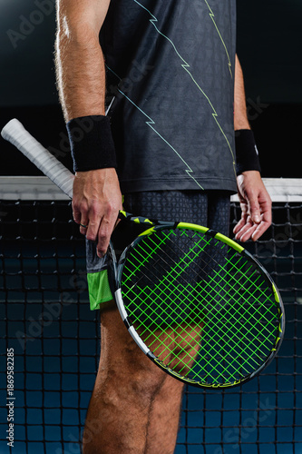 Midsection view of a male tennis player standing near the net holding a tennis racket on a blue court. Pause between points, focus, confidence and professional sport concept.