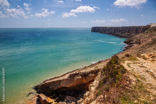A breathtaking panoramic view from the rugged cliffs of Sagres, Portugal, overlooking the vast turquoise waters of the Atlantic Ocean.