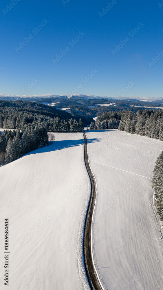 Obraz premium Winding road passing through deep snow in the Black Forest mountains, aerial view