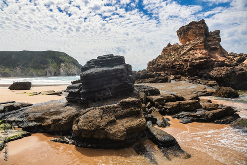 A breathtaking perspective of Praia do Castelejo in the Algarve, Portugal, where towering, stratified rock formations rise dramatically from the golden sands and turquoise waters. 