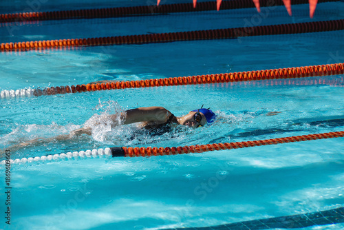 Female swimmer in swimsuit swimming front crawl in outdoor pool between orange lane dividers