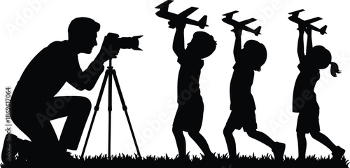 Silhouettes of a photographer with a camera on a tripod and three people holding model airplanes in a field
