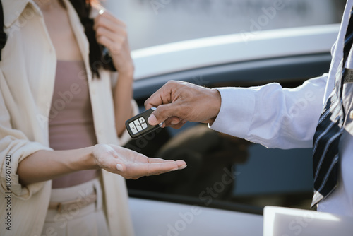 Obraz na plátně A man hands a car key to a woman beside a vehicle, symbolizing car rental, vehicle handover, customer service, and modern transportation agreement
