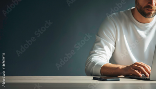 Young man working on a laptop at a clean modern desk, minimal workspace and dark background, concept of productivity and concentration.