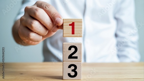 Hand placing wooden block number one on top of a stack, symbolizing priority or first step