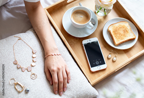 Cozy breakfast tray with coffee, toast, jewelry, and smartphone on bed
