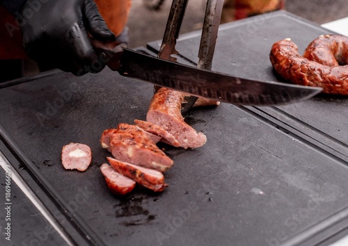 Male hands of a cook cutting sausage at a barbecue