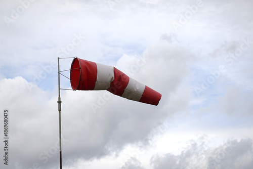 Red and white windsock indicating wind direction and speed approximate 6 knots against a cloudy sky on aerodrome airfield view close-up