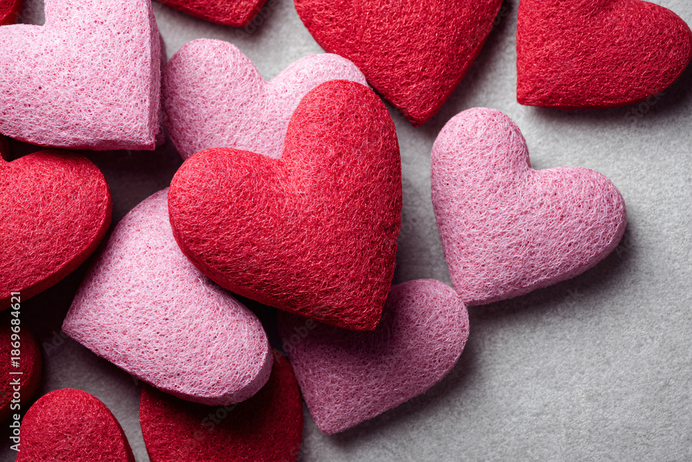 Obraz premium Close-up of textured red and pink hearts scattered on a grey background.