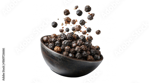Whole black peppercorns spilling from a dark bowl