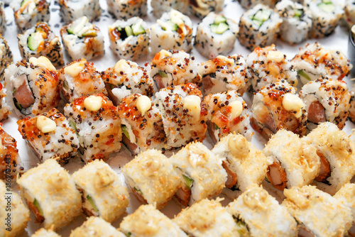 Valokuva Close-up of assorted sushi rolls arranged in rows, topped with sesame seeds, spicy sauce, and mayonnaise