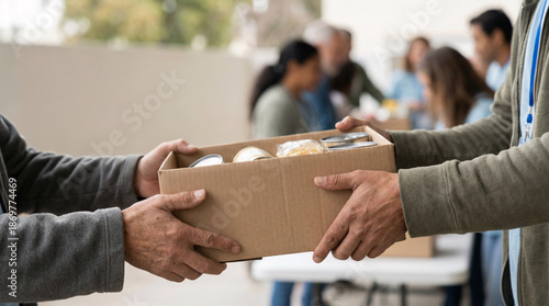 Hands passing donation box filled with canned goods and food items, symbolizing community support and volunteering