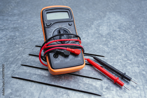 Canvas Print Orange digital multimeter with red test probe leads on textured gray metal background