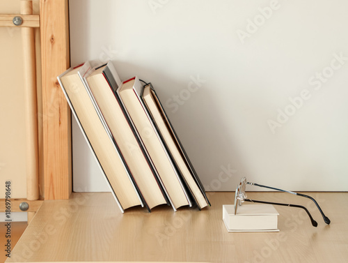 Fotografia Reading glasses placed on a bright wooden table next to a row of books