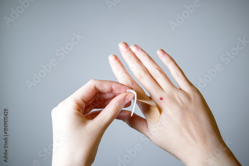 Bild auf Leinwand Female putting sticking plaster onto hand on gray background.