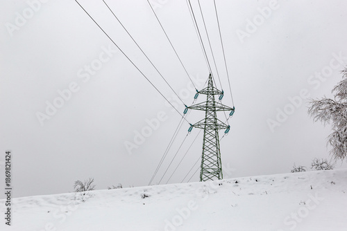High-voltage power lines on a cloudy winter day in a mountainous area.