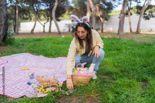 Canvas Print Woman organizing an easter picnic basket with decorated eggs on green grass