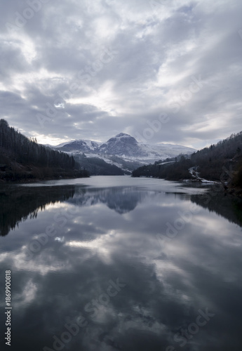 The majestic peak of Txindoki emerges from the winter clouds above the cold waters of the Ibiur reservoir.