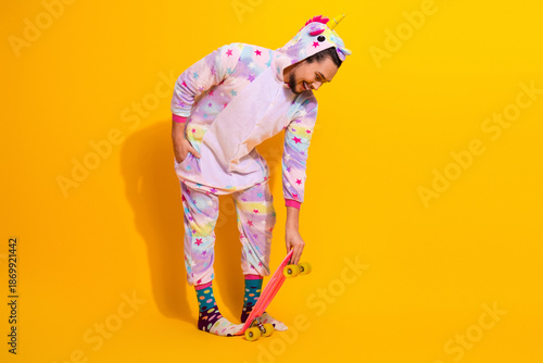 Canvas-taulu Playful unicorn pajama wearing man riding a skateboard in a bright yellow studio