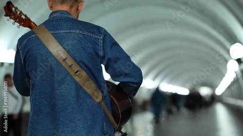 Street musician busking in subway tunnel playing acoustic guitar for passersby