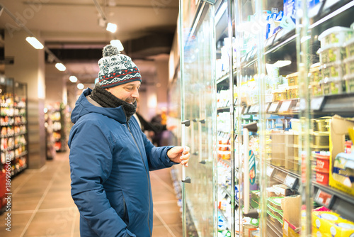 Fotografie Man wearing a winter hat and jacket smiling while choosing products from a refri