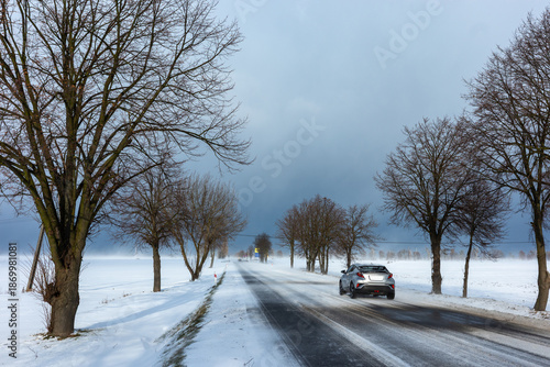 Country road in the winter during the snow blizzard. Road surfece covered with snow and ice. Dangerous car travel condition.