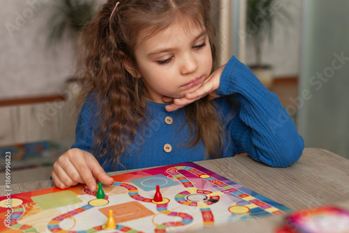 Portrait of little girl 5 years old with interest looks at board game