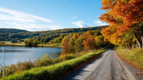 Serene landscape featuring peaceful lake bordered by colorful autumn trees alongside gravel road, bright blue sky, seasonal countryside scene, with copy space
