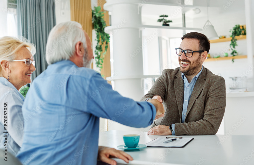 Fototapeta premium Portrait of a businessman or real estate agent or doctor shaking hands and signing a deal contract with senior couple in his office