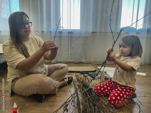 Mother and daughter enjoy creative bonding making an art project from natural twigs on the floor, fostering creativity and education through handmade crafts in a domestic setting.