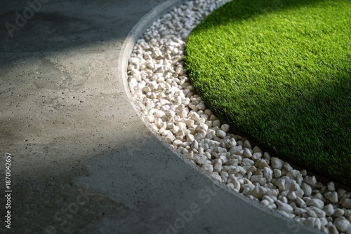 Modern landscaped garden with green artificial grass, white pebbles, and a smooth concrete border creates a peaceful outdoor aesthetic