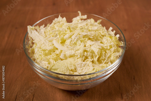 A glass bowl with sliced Chinese cabbage stands on a wooden table.
