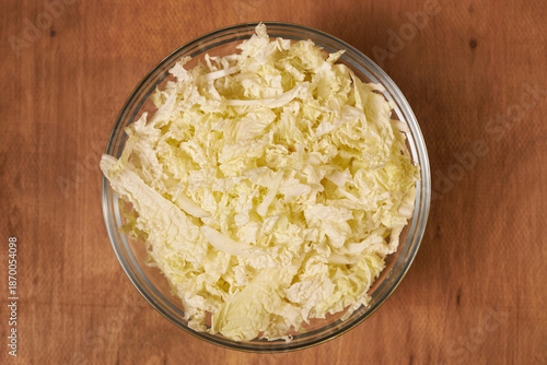 A glass bowl with sliced Chinese cabbage stands on a wooden table.