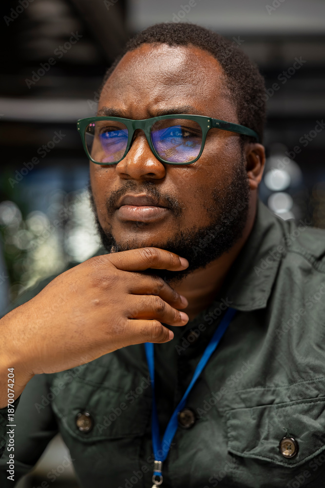 Obraz premium Black general manager envisioning rational solution and scratching his chin, works after hours at desk. Man engaging in critical thinking, evaluating each option for a different perspective.