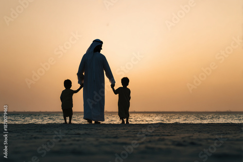 Emirati father and his sons wearing traditional dress walking on the beach with Dubai, Burj Khalifa and Burj Al Arab in the background, Happy family spending a wonderful day. picnic. Arab family.