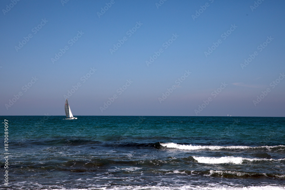 Obraz premium sailboat on the sea, Rocky Shoreline and Breakwater under Clear Blue Sky