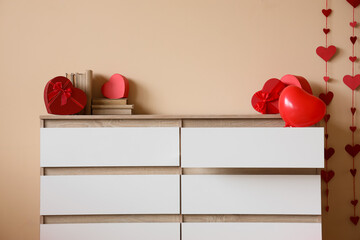 Chest of drawers with books and gifts for Valentine's Day near beige wall