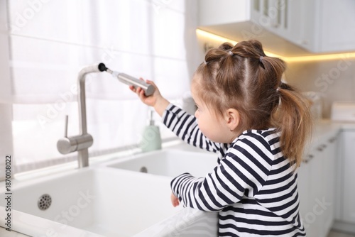 Child safety at home. Little girl pulling down faucet hose at sink in kitchen